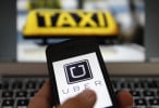 An illustration picture shows the logo of car-sharing service app Uber on a móvil next to the picture of an official German taxi sign