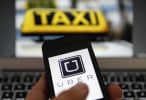 An illustration picture shows the logo of car-sharing service app Uber on a celular next to the picture of an official German taxi sign