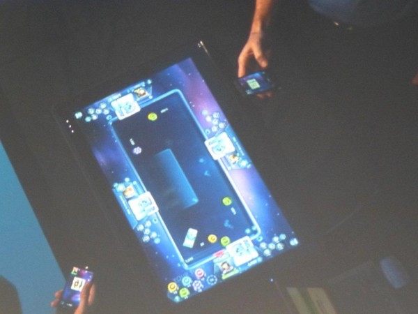 Una mesa de poker virtual. En la pantalla grande se ve la mesa con las cartas boca abajo y en la mano, cada jugador con su smartphone puede ver sus cartas.